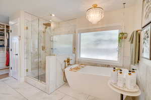 Bathroom with an inviting chandelier, shower with separate bathtub, and tile walls