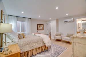 Bedroom with connected bathroom, light hardwood / wood-style flooring, and an AC wall unit