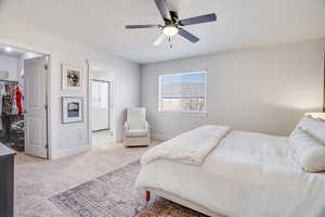 Bedroom featuring a spacious closet, light colored carpet, a textured ceiling, ensuite bath, and a closet