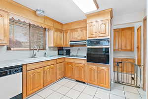 Kitchen featuring light tile patterned flooring, range hood, sink, and black appliances