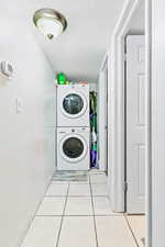 Laundry room with light tile patterned floors, a textured ceiling, and stacked washer / dryer