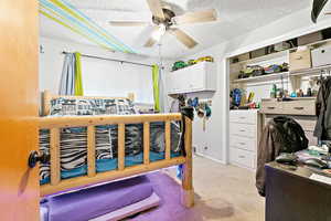 Carpeted bedroom featuring ceiling fan, a closet, and a textured ceiling