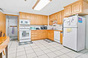 Kitchen featuring light brown cabinetry, sink, white appliances, and light tile patterned flooring