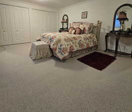 Bedroom with two closets, carpet floors, and ornamental molding