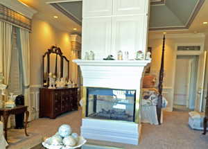 Sitting room with a multi sided fireplace, ornamental molding, and light colored carpet