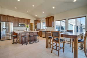 Kitchen featuring a breakfast bar, appliances with stainless steel finishes, a center island, light stone counters, and vaulted ceiling