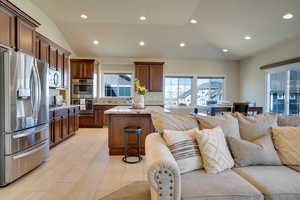 Kitchen with a breakfast bar, a center island, vaulted ceiling, stainless steel appliances, and light stone countertops