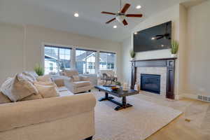 Carpeted living room with ceiling fan, lofted ceiling, and a fireplace