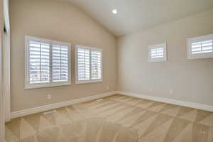 Spare room with lofted ceiling, a wealth of natural light, and light colored carpet