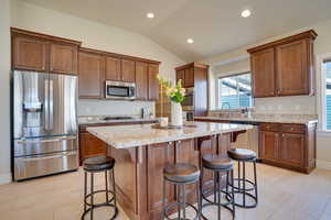 Kitchen with a kitchen island, lofted ceiling, a kitchen bar, light stone counters, and stainless steel appliances