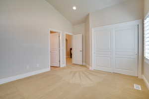 Unfurnished bedroom with light colored carpet, high vaulted ceiling, and a closet