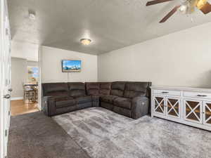 Carpeted living room with ceiling fan, a textured ceiling, and lofted ceiling