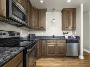 Kitchen with decorative light fixtures, stainless steel appliances, dark stone countertops, sink, and light wood-type flooring