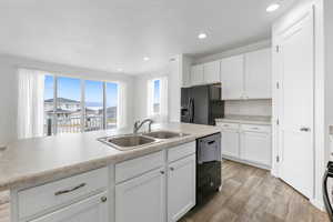 Kitchen with sink, white cabinets, a kitchen island with sink, black appliances, and light hardwood / wood-style flooring