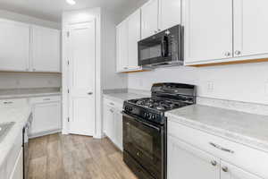 Kitchen with light hardwood / wood-style flooring, white cabinets, and black appliances