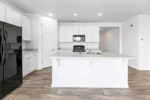 Kitchen featuring white cabinets, sink, a kitchen island with sink, and black appliances