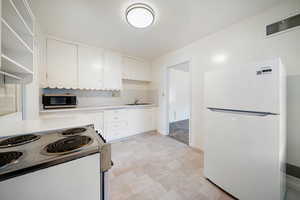 Kitchen featuring white cabinetry, sink, and white appliances