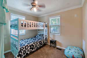 Carpeted bedroom with multiple windows, ornamental molding, and a textured ceiling