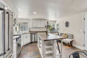 Kitchen featuring appliances with stainless steel finishes, sink, white cabinets, backsplash, and a textured ceiling