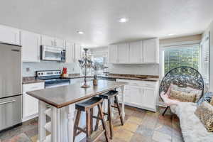 Kitchen featuring tasteful backsplash, appliances with stainless steel finishes, a kitchen breakfast bar, and white cabinets