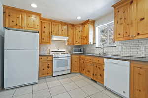 Kitchen featuring tasteful backsplash, sink, white appliances, and light tile patterned floors