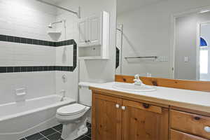 Full bathroom with tile patterned flooring, vanity, tiled shower / bath combo, and toilet