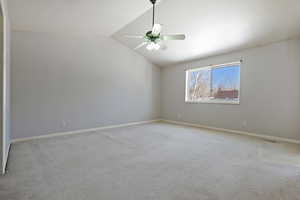 Carpeted spare room featuring ceiling fan and vaulted ceiling