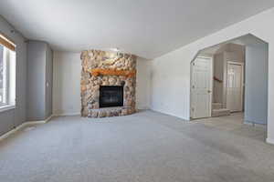 Unfurnished living room featuring a stone fireplace, a healthy amount of sunlight, and light carpet