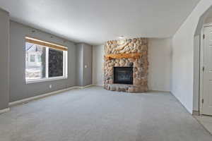 Unfurnished living room with a stone fireplace and light carpet