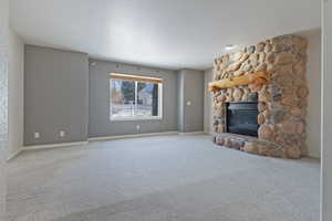 Unfurnished living room featuring a stone fireplace and carpet flooring