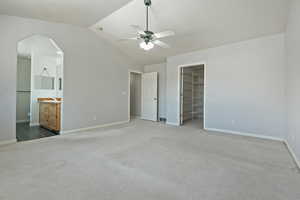 Unfurnished bedroom with ensuite bath, a spacious closet, dark carpet, vaulted ceiling, and a closet