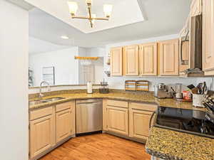 Kitchen with sink, appliances with stainless steel finishes, light hardwood / wood-style floors, stone countertops, and light brown cabinets