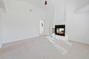 Unfurnished living room with a multi sided fireplace, light colored carpet, ceiling fan, and high vaulted ceiling