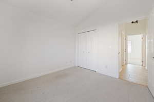 Unfurnished bedroom featuring high vaulted ceiling, light colored carpet, and a closet