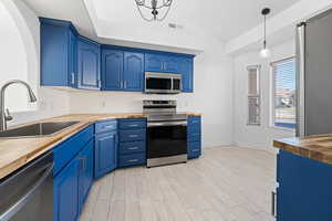 Kitchen featuring appliances with stainless steel finishes, pendant lighting, blue cabinets, butcher block counters, and sink