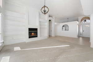 Unfurnished living room featuring light carpet, an inviting chandelier, and built in shelves