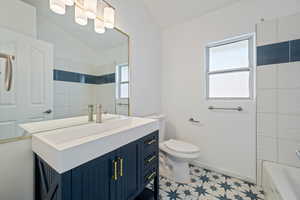 Full bathroom featuring vaulted ceiling, vanity, plenty of natural light, and toilet