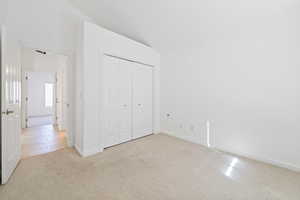 Unfurnished bedroom with light carpet, lofted ceiling, and a closet