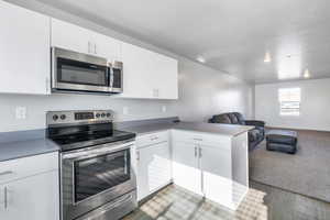 Kitchen featuring wood-type flooring, kitchen peninsula, white cabinets, and appliances with stainless steel finishes