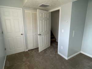 Unfurnished bedroom featuring dark carpet, a closet, and a textured ceiling