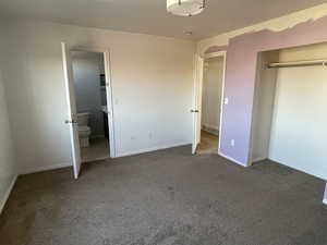 Unfurnished bedroom featuring ensuite bathroom and dark carpet