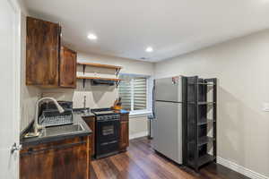 Kitchen with black / electric stove, dark hardwood / wood-style floors, sink, and stainless steel refrigerator