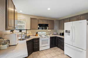 Kitchen with white appliances, sink, dark brown cabinets, and light tile patterned floors