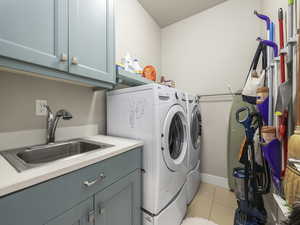 Clothes washing area featuring cabinets, sink, washing machine and dryer, and light tile patterned floors