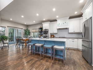 Kitchen with a breakfast bar, an island with sink, white cabinets, dark hardwood / wood-style flooring, and stainless steel appliances