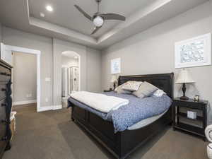 Carpeted bedroom featuring connected bathroom, a tray ceiling, and ceiling fan