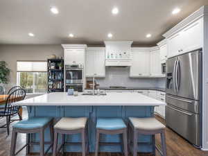 Kitchen featuring appliances with stainless steel finishes, dark hardwood / wood-style floors, sink, white cabinets, and a kitchen island with sink