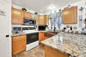 Kitchen with light stone countertops, sink, and electric range