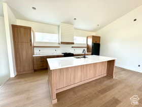 Kitchen with lofted ceiling, sink, black refrigerator, a center island, and light wood-type flooring