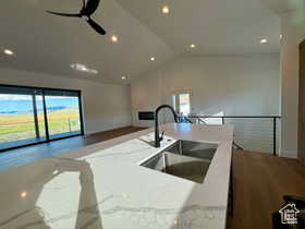 Kitchen with lofted ceiling, sink, wood-type flooring, ceiling fan, and light stone countertops